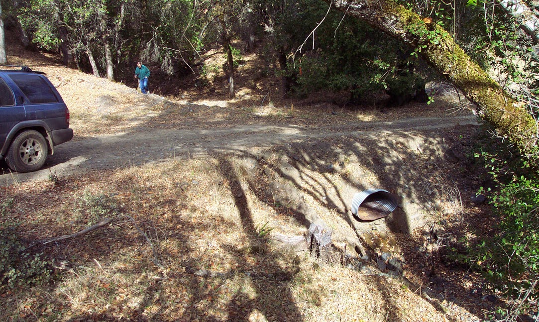 A dirt road has a culvert (that looks squashed) for a stream crossing zone. 