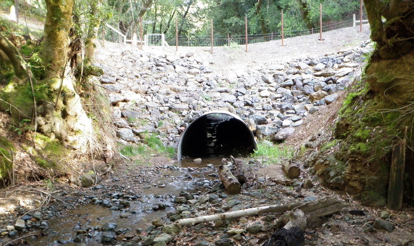 One much larger culvert is shown at the same location, this time with a clear view from one side of the road to another, showing how water can easily flow under the road through this larger culvert.